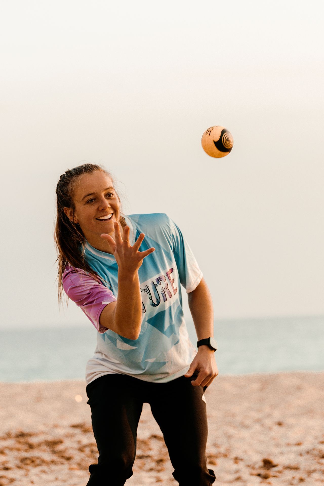 Person playing catch on a beach, wearing a sporty shirt and wristwatch.