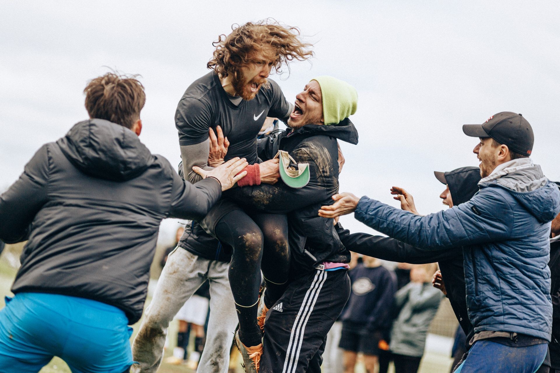 Group of men celebrating and embracing each other passionately outdoors, likely after a sports victory.