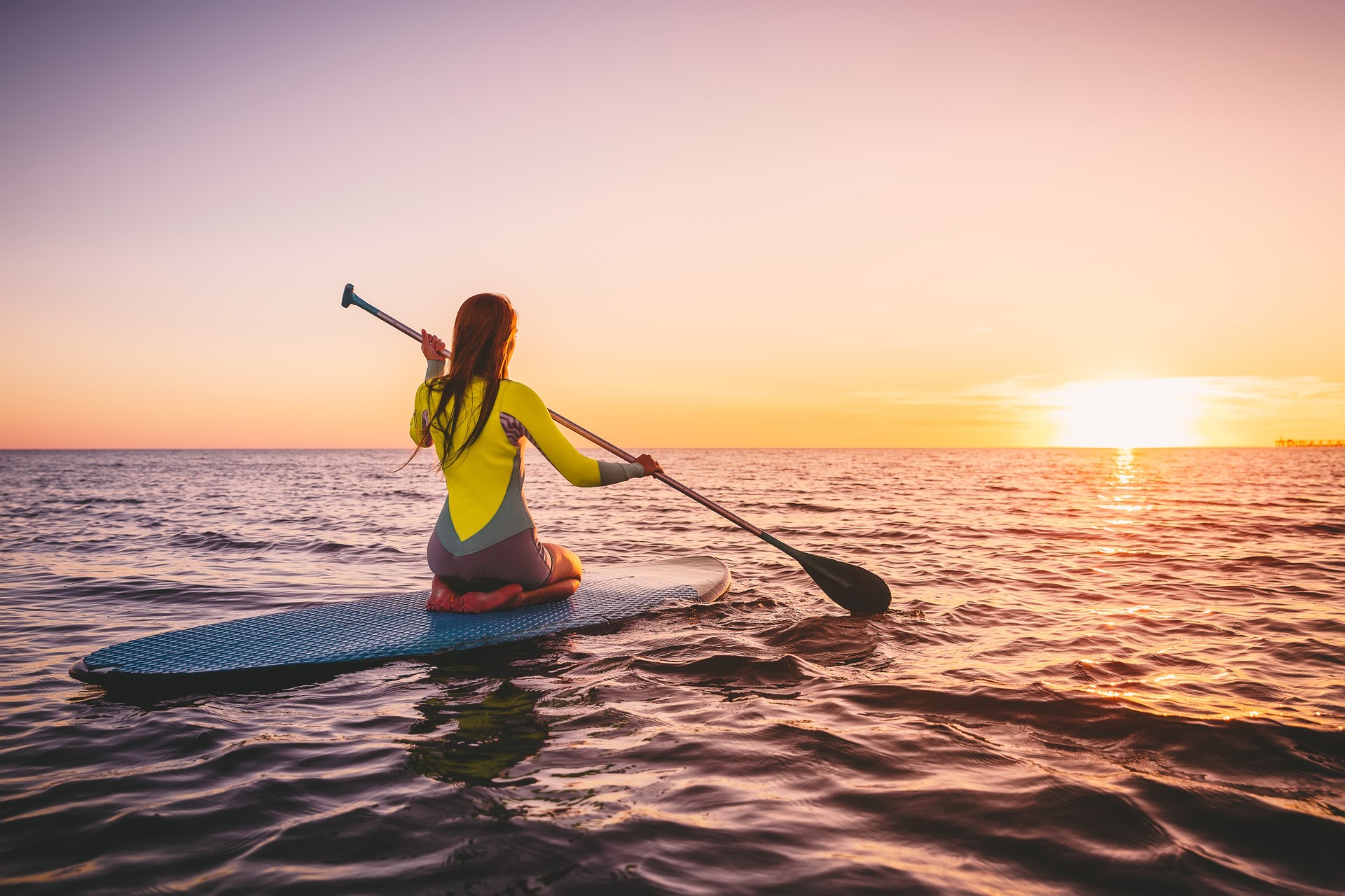 Girl on stand up paddle board, quiet sea with warm sunset colors. Relaxing on ocean